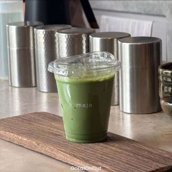 แก้วมัทฉะเย็นวางบนแผ่นไม้ที่เคาน์เตอร์บาร์ร้าน maja. Matcha House