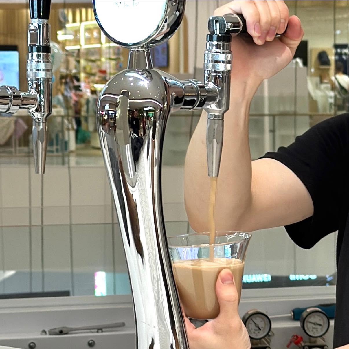 พนักงานกำลังกดชาไนโตร Velvet Milk Tea จากแท็ปเครื่องดื่มลงในแก้ว